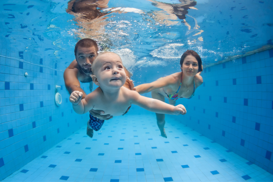 Bebé bajo el agua nadando con su padre y madre en una pisina
